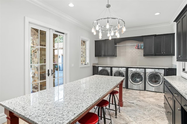 clothes washing area with cabinets, washing machine and dryer, crown molding, and a notable chandelier