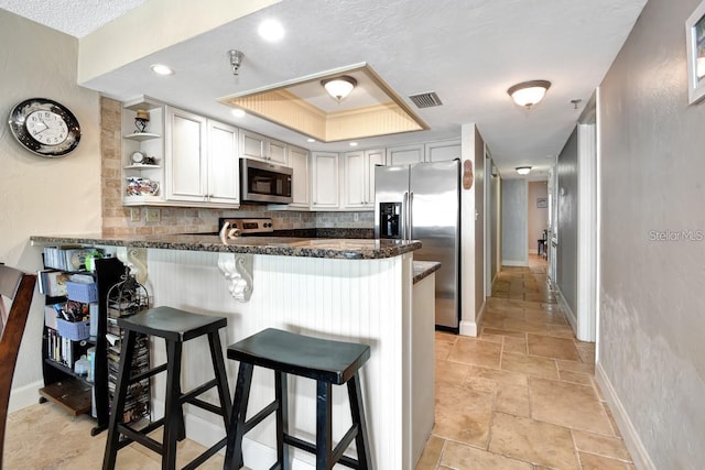 kitchen with a kitchen bar, kitchen peninsula, backsplash, and appliances with stainless steel finishes