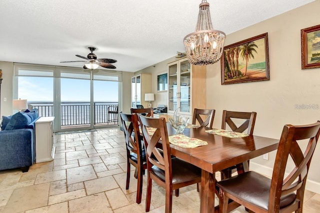 dining area with ceiling fan with notable chandelier, a water view, a wall of windows, and a textured ceiling