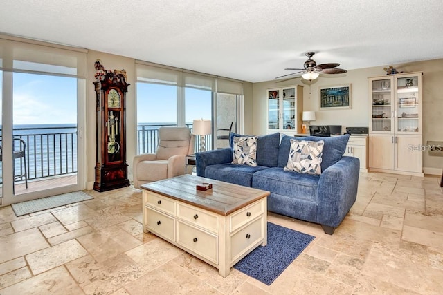 living room featuring ceiling fan, plenty of natural light, a water view, and a textured ceiling