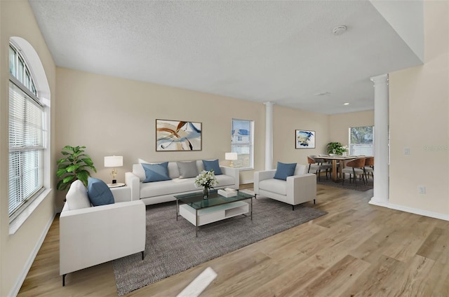 living room featuring ornate columns, light hardwood / wood-style flooring, and a textured ceiling