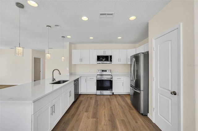 kitchen with kitchen peninsula, appliances with stainless steel finishes, sink, white cabinetry, and hanging light fixtures