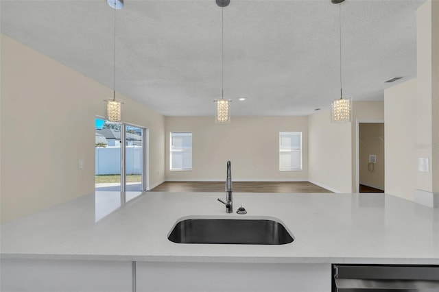 kitchen featuring a textured ceiling, decorative light fixtures, sink, and dishwashing machine