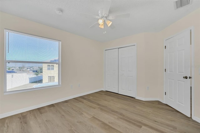 unfurnished bedroom featuring a textured ceiling, a closet, light hardwood / wood-style floors, and ceiling fan