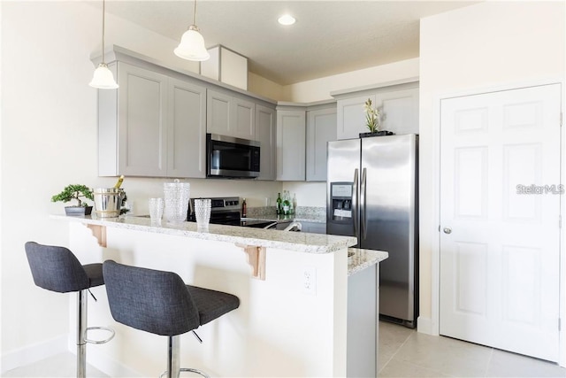 kitchen with a kitchen breakfast bar, decorative light fixtures, a peninsula, stainless steel appliances, and gray cabinetry