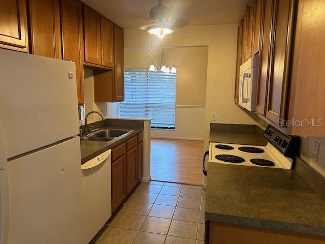 kitchen with light tile patterned flooring, white appliances, ceiling fan with notable chandelier, and sink