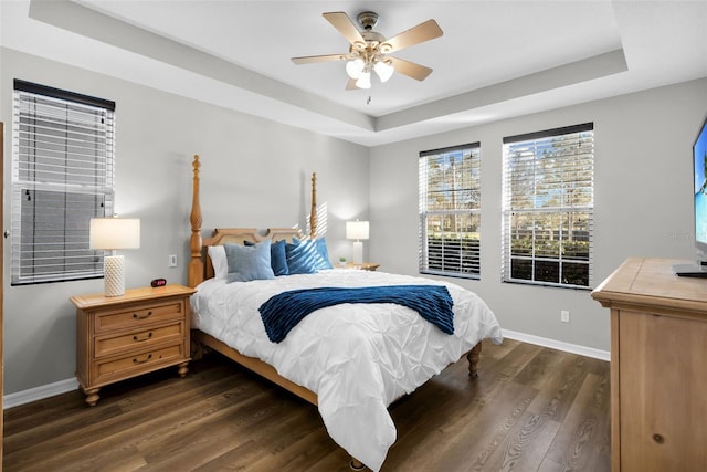 bedroom with a tray ceiling, ceiling fan, and dark wood-type flooring