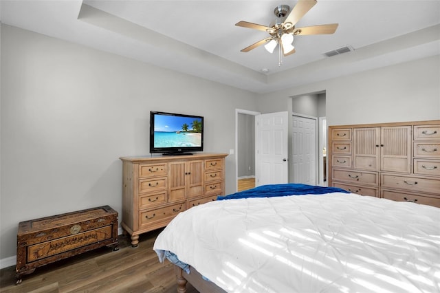 bedroom with dark hardwood / wood-style flooring, a closet, a raised ceiling, and ceiling fan