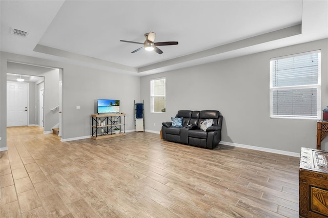 living area featuring a raised ceiling, ceiling fan, and light wood-type flooring