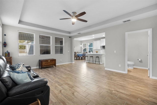 living room with a raised ceiling, ceiling fan, and light hardwood / wood-style floors