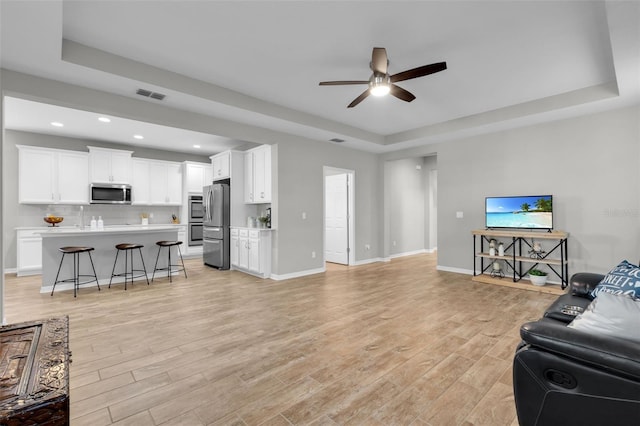 living room with ceiling fan, light hardwood / wood-style flooring, and a tray ceiling