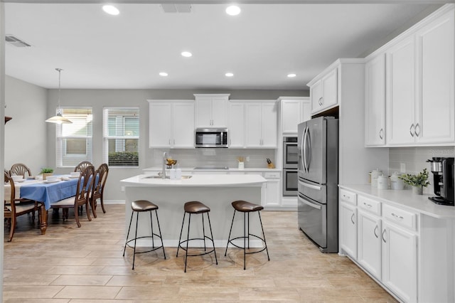 kitchen featuring white cabinets, stainless steel appliances, a kitchen island with sink, and tasteful backsplash