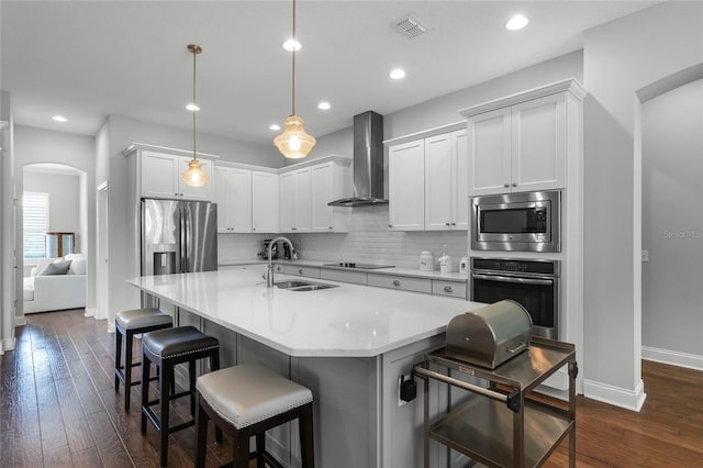 kitchen featuring a kitchen island with sink, a breakfast bar, stainless steel appliances, and wall chimney range hood