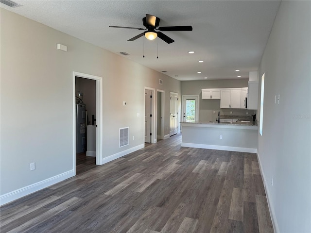 unfurnished living room with a textured ceiling, ceiling fan, sink, and dark wood-type flooring