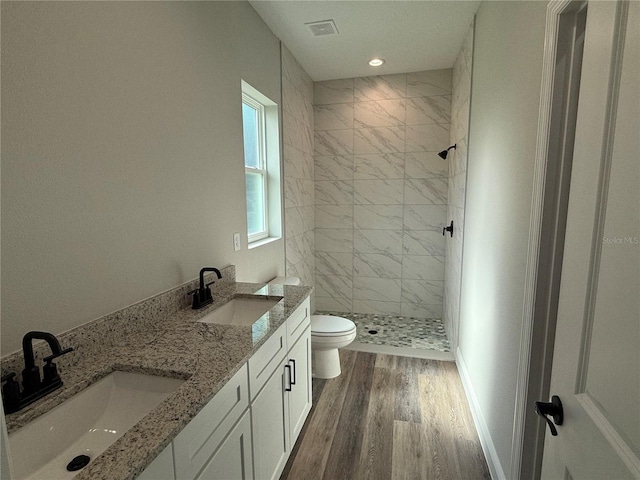 bathroom with a tile shower, hardwood / wood-style floors, vanity, and toilet