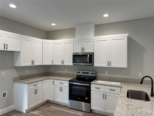 kitchen with dark hardwood / wood-style flooring, light stone counters, stainless steel appliances, sink, and white cabinetry