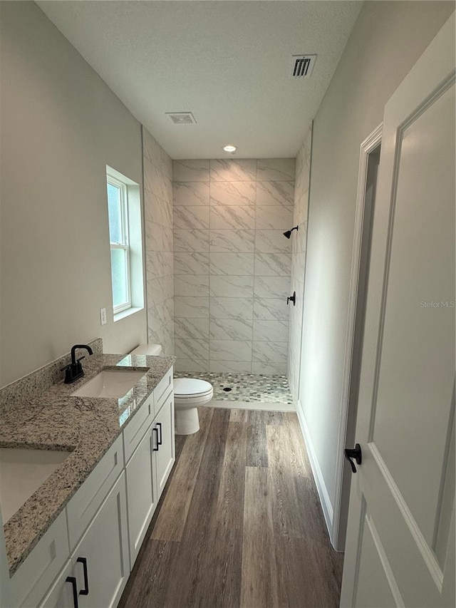 bathroom featuring a textured ceiling, tiled shower, toilet, vanity, and hardwood / wood-style flooring