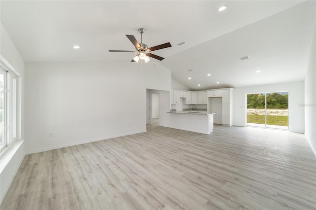 unfurnished living room with ceiling fan, vaulted ceiling, sink, and light hardwood / wood-style flooring