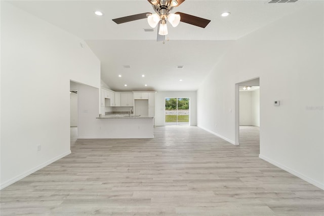 unfurnished living room featuring ceiling fan, light wood-type flooring, sink, and high vaulted ceiling