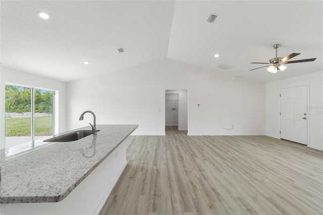 kitchen with light stone countertops, sink, ceiling fan, a kitchen island with sink, and light wood-type flooring