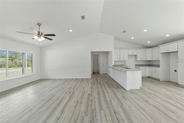 kitchen featuring white cabinets, light wood-type flooring, vaulted ceiling, and light stone countertops