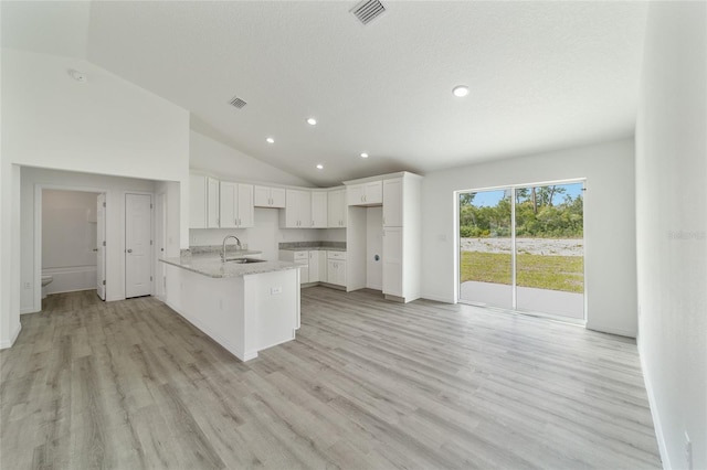 kitchen featuring white cabinets, light stone counters, lofted ceiling, and sink