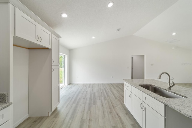 kitchen with light stone counters, vaulted ceiling, sink, light hardwood / wood-style floors, and white cabinetry