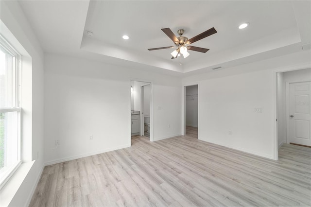 unfurnished bedroom with a raised ceiling, light hardwood / wood-style flooring, ceiling fan, a spacious closet, and a closet