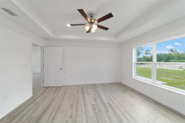 unfurnished room with a raised ceiling, ceiling fan, and light hardwood / wood-style flooring