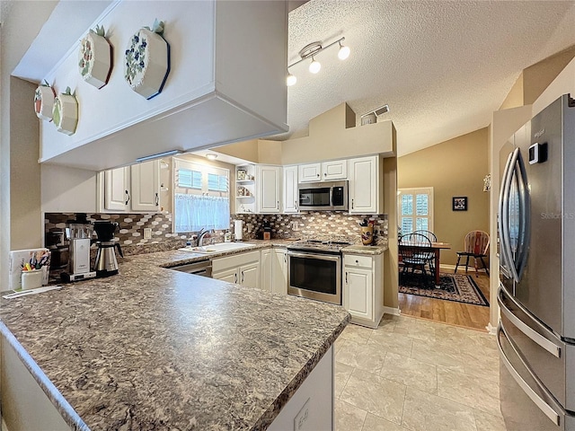 kitchen featuring white cabinetry, sink, stainless steel appliances, kitchen peninsula, and lofted ceiling