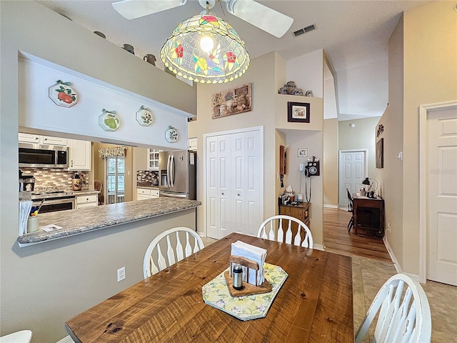 dining area with ceiling fan, a towering ceiling, and light hardwood / wood-style flooring