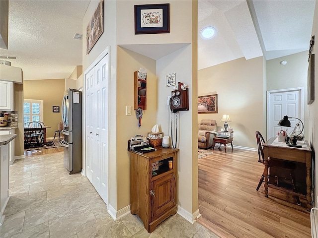 hall featuring a textured ceiling, light wood-type flooring, and vaulted ceiling