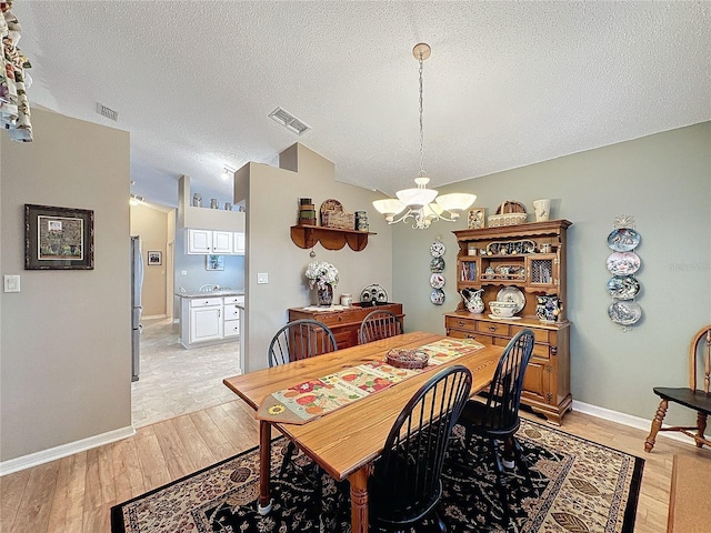 dining room featuring a textured ceiling, light wood-type flooring, an inviting chandelier, and lofted ceiling