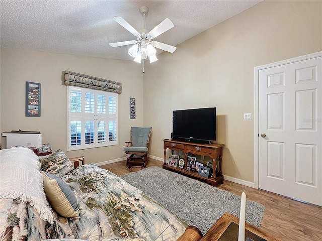 bedroom with a textured ceiling, hardwood / wood-style flooring, ceiling fan, and lofted ceiling