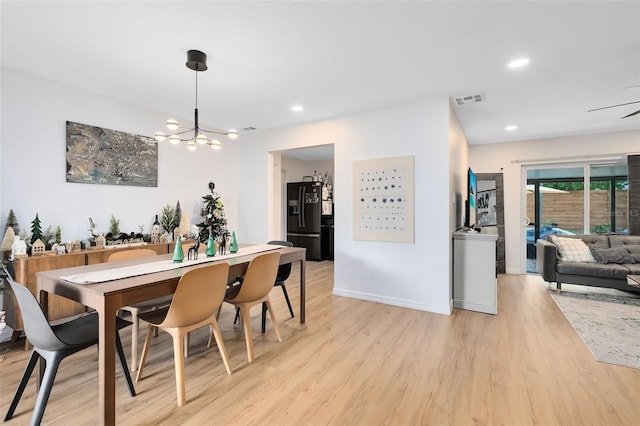 dining area with ceiling fan with notable chandelier and light hardwood / wood-style flooring