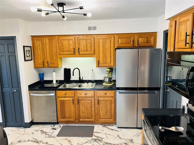 kitchen with sink, a notable chandelier, stainless steel appliances, and a textured ceiling