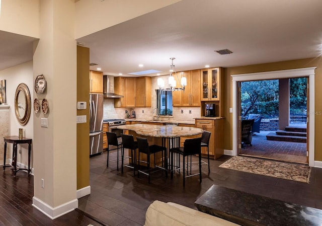 kitchen featuring appliances with stainless steel finishes, wall chimney exhaust hood, sink, a center island, and hanging light fixtures