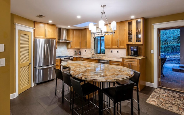 kitchen featuring decorative backsplash, appliances with stainless steel finishes, wall chimney exhaust hood, sink, and pendant lighting