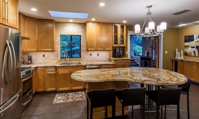 kitchen featuring a skylight, light stone countertops, sink, stainless steel appliances, and hanging light fixtures