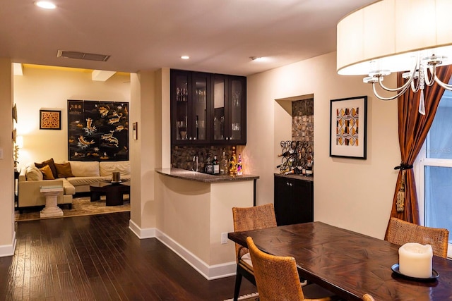 bar with decorative backsplash, dark hardwood / wood-style flooring, dark brown cabinets, and a chandelier