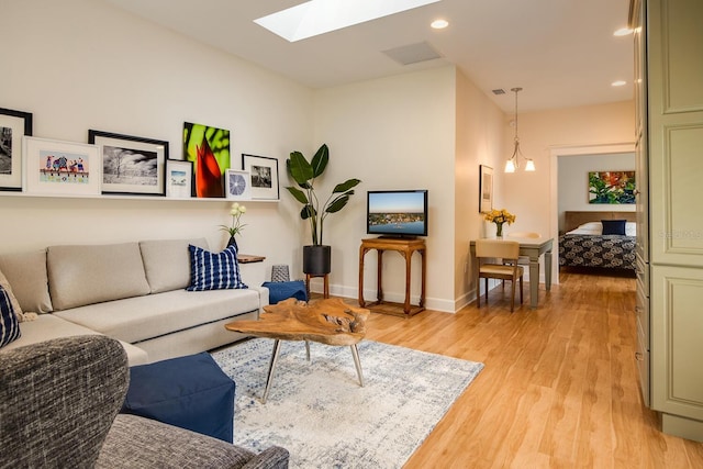 living room featuring a chandelier, light hardwood / wood-style floors, and a skylight