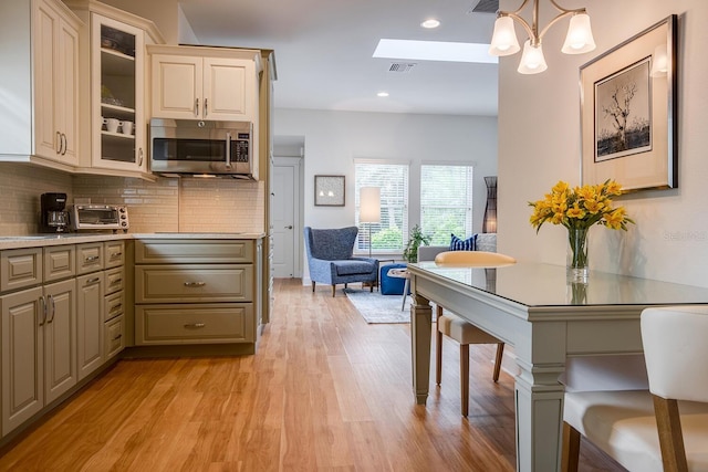 kitchen with backsplash, hanging light fixtures, a skylight, light wood-type flooring, and cream cabinetry