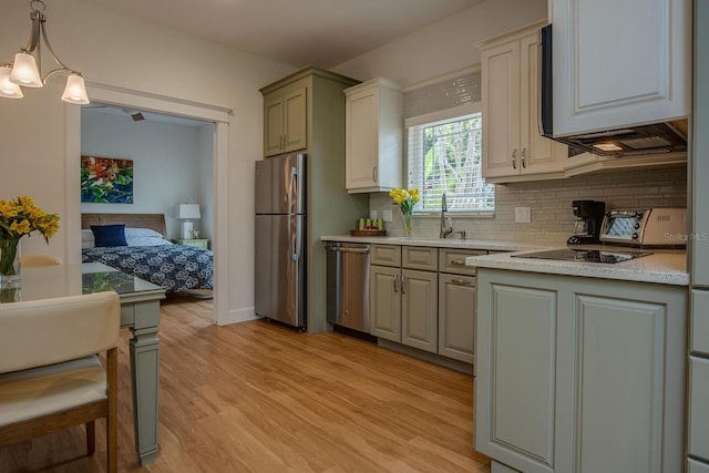 kitchen with backsplash, stainless steel appliances, sink, decorative light fixtures, and light hardwood / wood-style floors