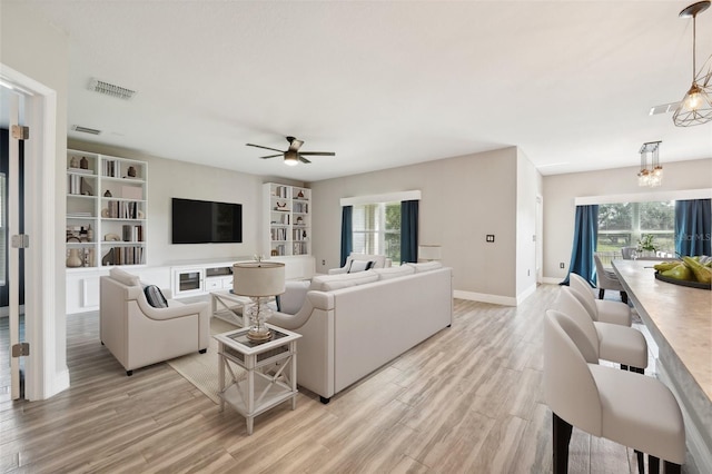 living room featuring ceiling fan with notable chandelier and light wood-type flooring