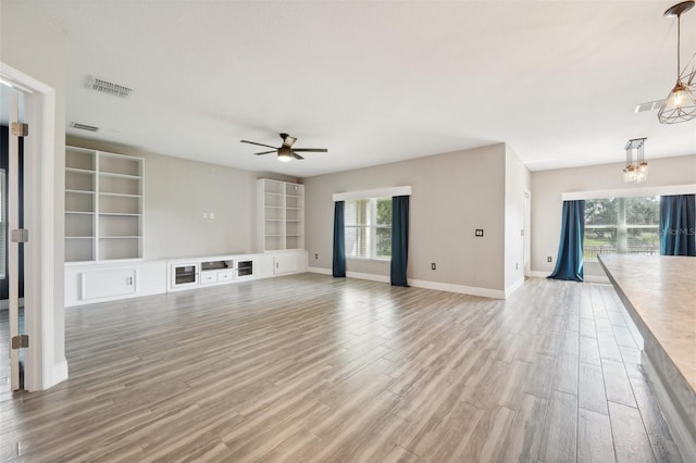 unfurnished living room featuring ceiling fan with notable chandelier and light hardwood / wood-style flooring