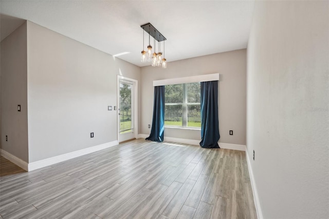 empty room with light wood-type flooring and a notable chandelier