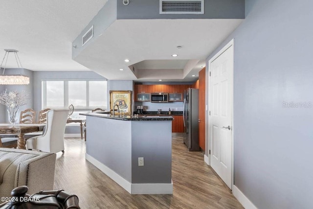 kitchen with an inviting chandelier, a raised ceiling, appliances with stainless steel finishes, decorative light fixtures, and wood-type flooring