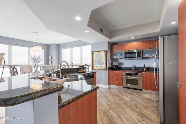 kitchen featuring appliances with stainless steel finishes, sink, decorative light fixtures, light hardwood / wood-style flooring, and dark stone countertops