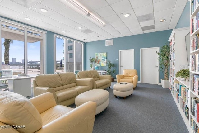 carpeted living room with a drop ceiling and a wall of windows