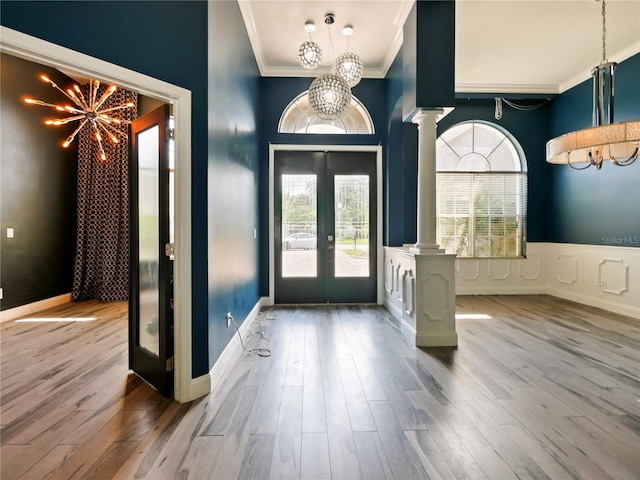 entrance foyer featuring crown molding, hardwood / wood-style flooring, an inviting chandelier, french doors, and ornate columns